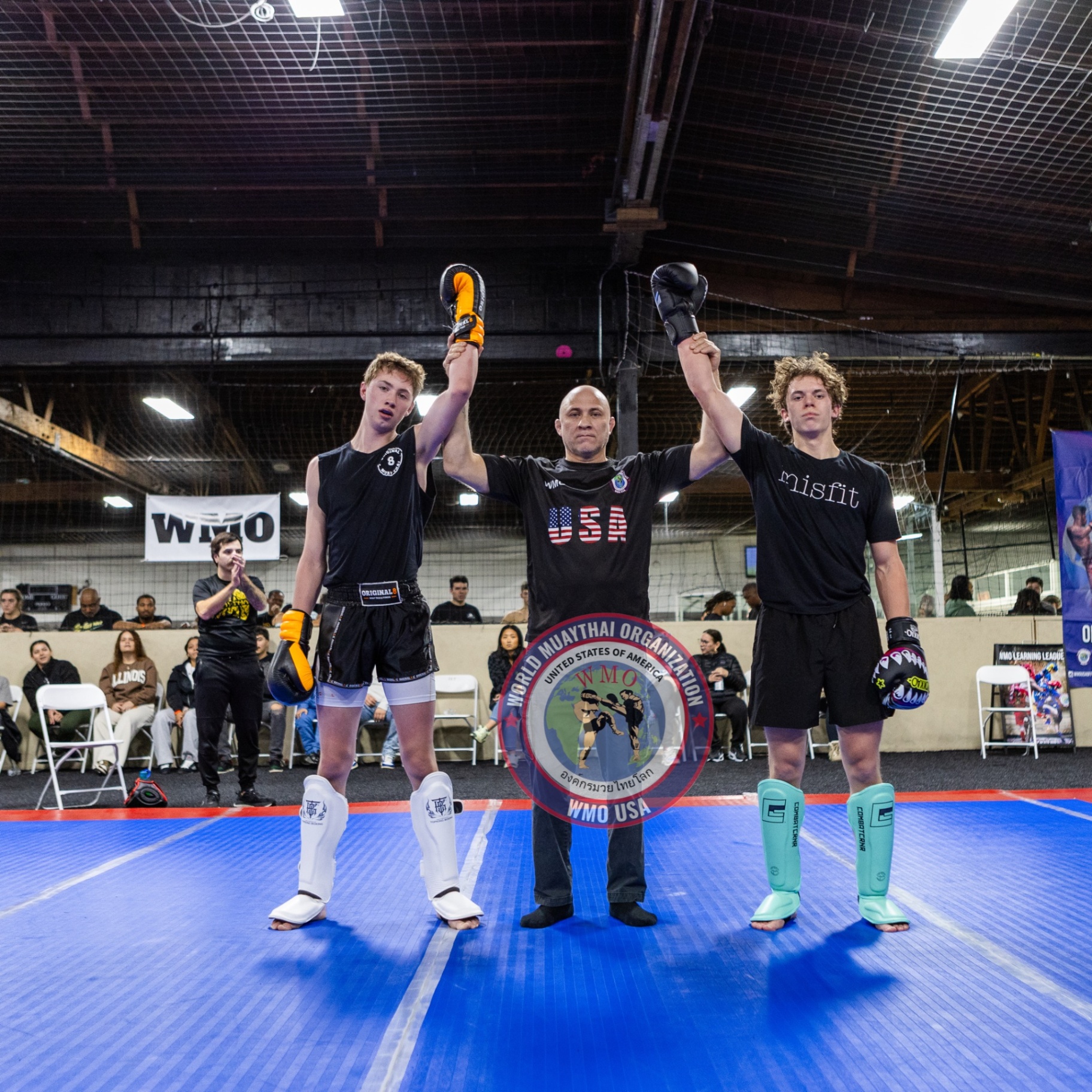 Referee raising the hands of two young fighters after a fair bout